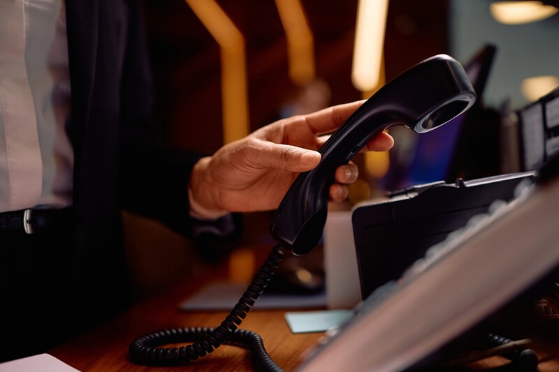 Close up of receptionist answering a phone call while working at hotel front desk.