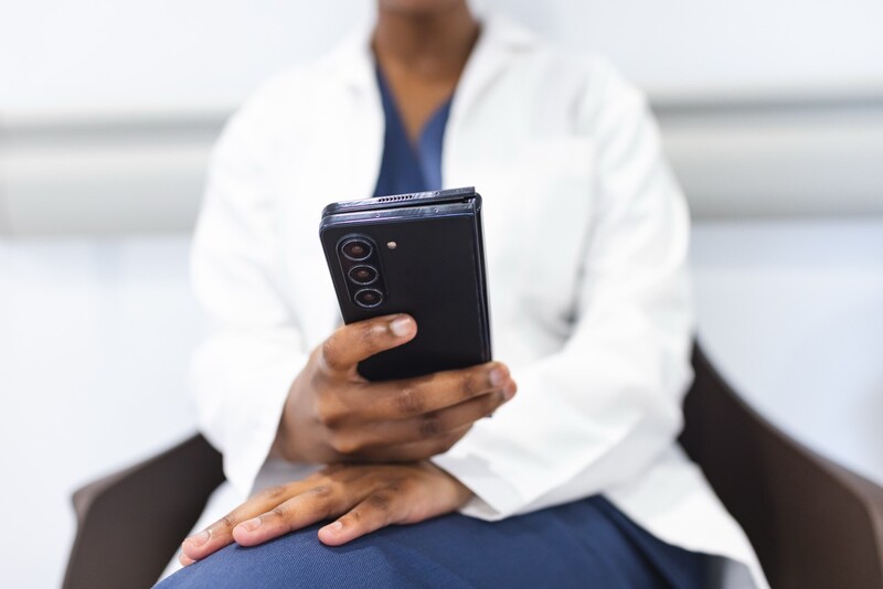 Midsection of african american female doctor using smartphone in waiting room in hospital. Medicine, healthcare, communication, work and hospital.