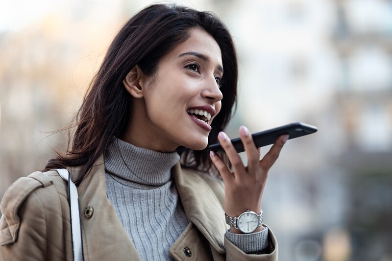 Shot of young woman using voice recognition system on her smartphone while standing in the street.